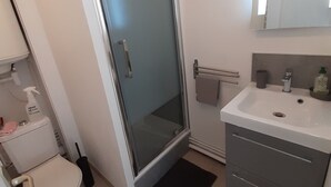 Ein Badezimmer mit Duschabtrennung aus Glas, Toilette, Waschbecken mit Spiegel und Handtuchhalter.