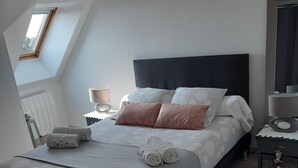 Ein Schlafzimmer mit Bett, Kissen, Nachttisch, Lampe, Spiegel und Fenster.