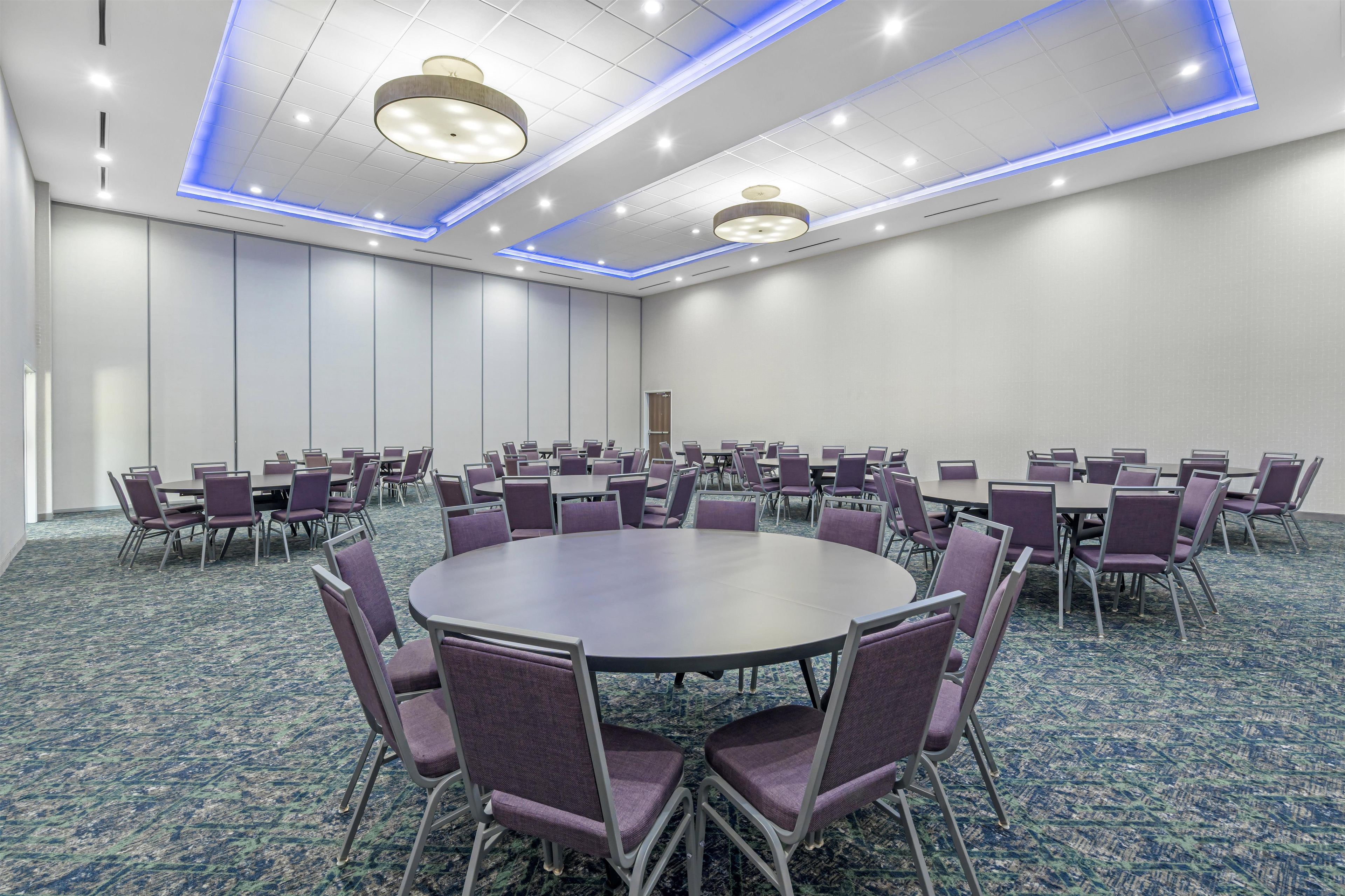Un salón de conferencias con mesas y sillas redondas, alfombra estampada e iluminación empotrada.