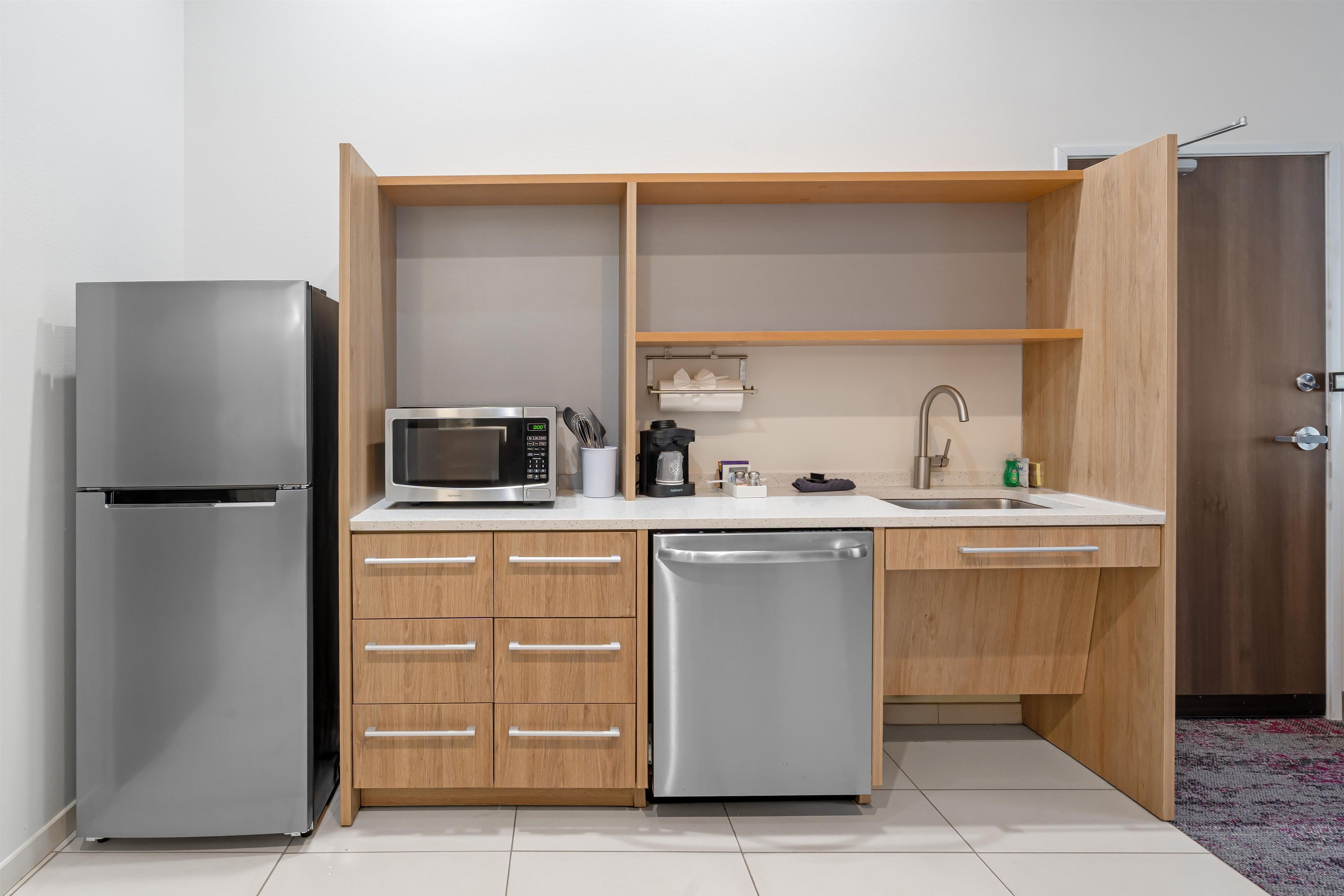 A compact kitchen with a refrigerator, microwave, dishwasher, and wooden cabinets.