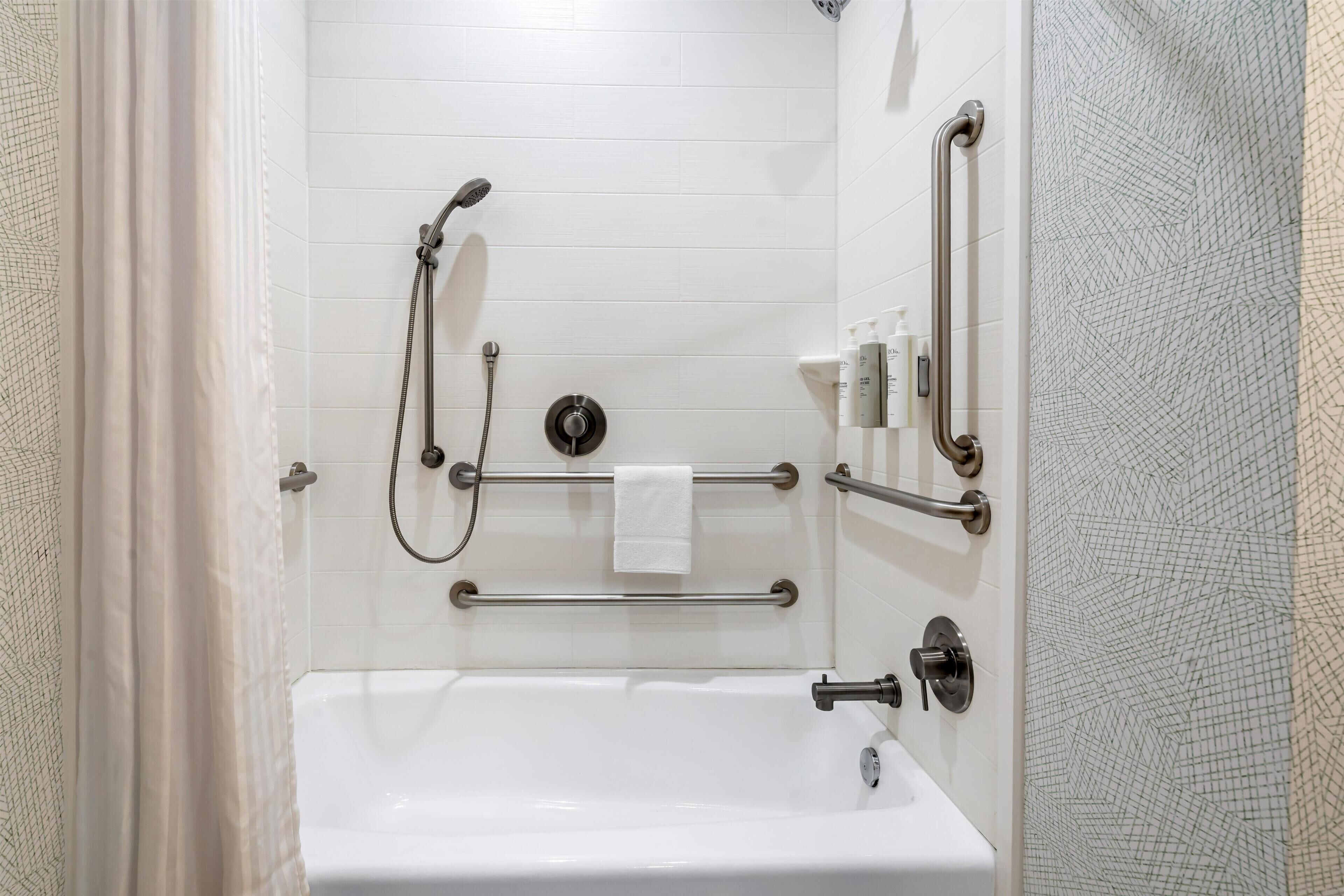 A bathroom with a white bathtub, grab bars, a handheld showerhead, and a towel rack.
