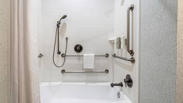 A bathroom with a white bathtub, grab bars, a handheld showerhead, and a towel rack.