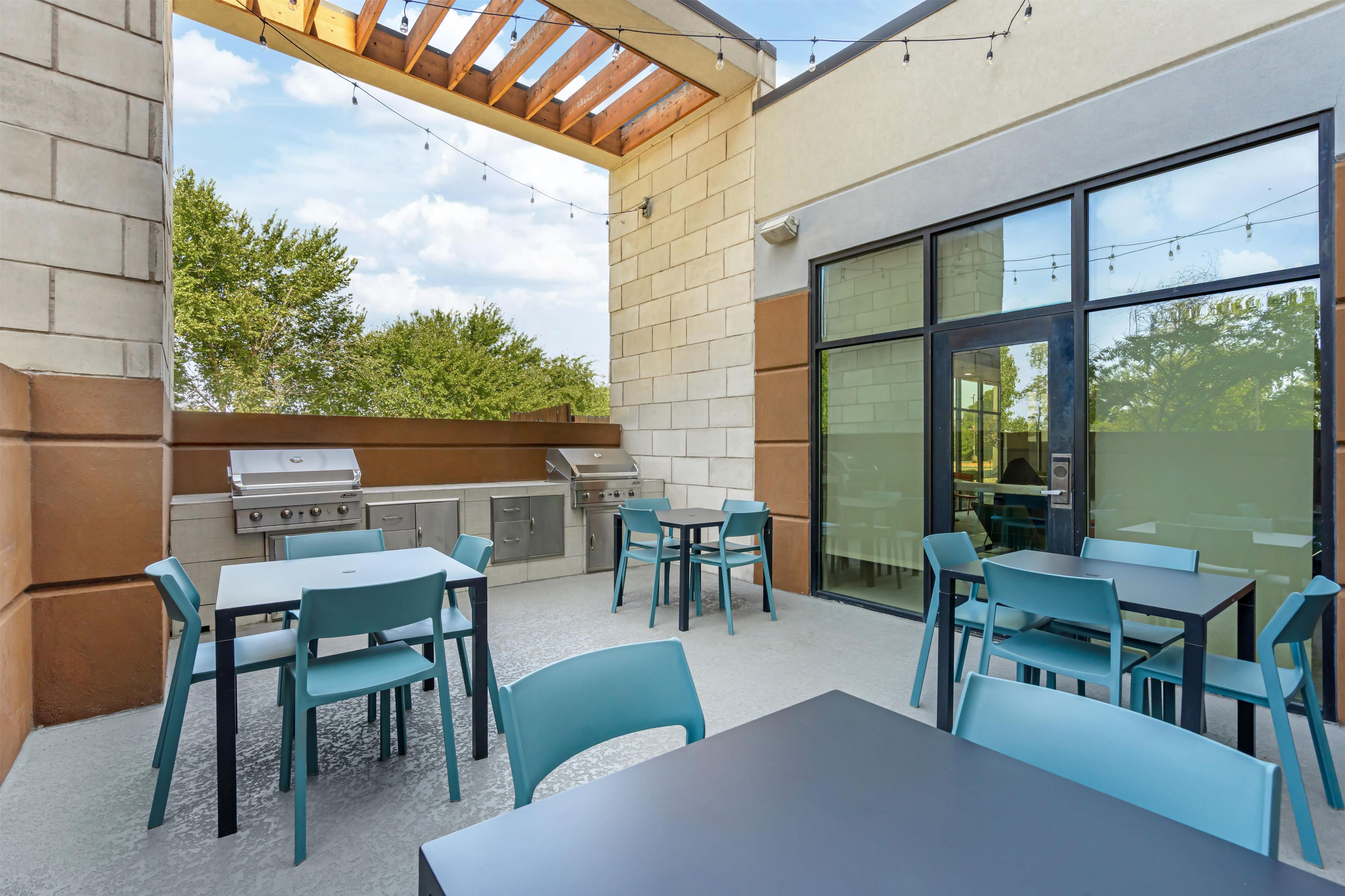 An outdoor patio area with a grill, tables, and chairs.