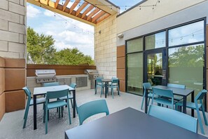 Een buitenterras met een barbecue, tafels en stoelen.