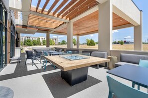 An outdoor patio area with a wooden table, seating, and a view of buildings in the background. - Home2 Suites by Hilton Dallas DeSoto (DeSoto)