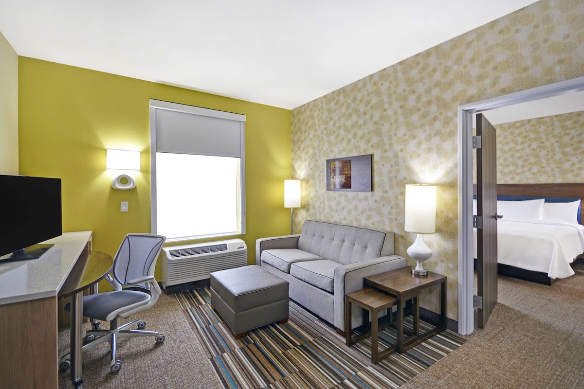 Une chambre d’hôtel équipée d’un bureau, d’un fauteuil de bureau, d’un canapé, d’un pouf et d’un lit.