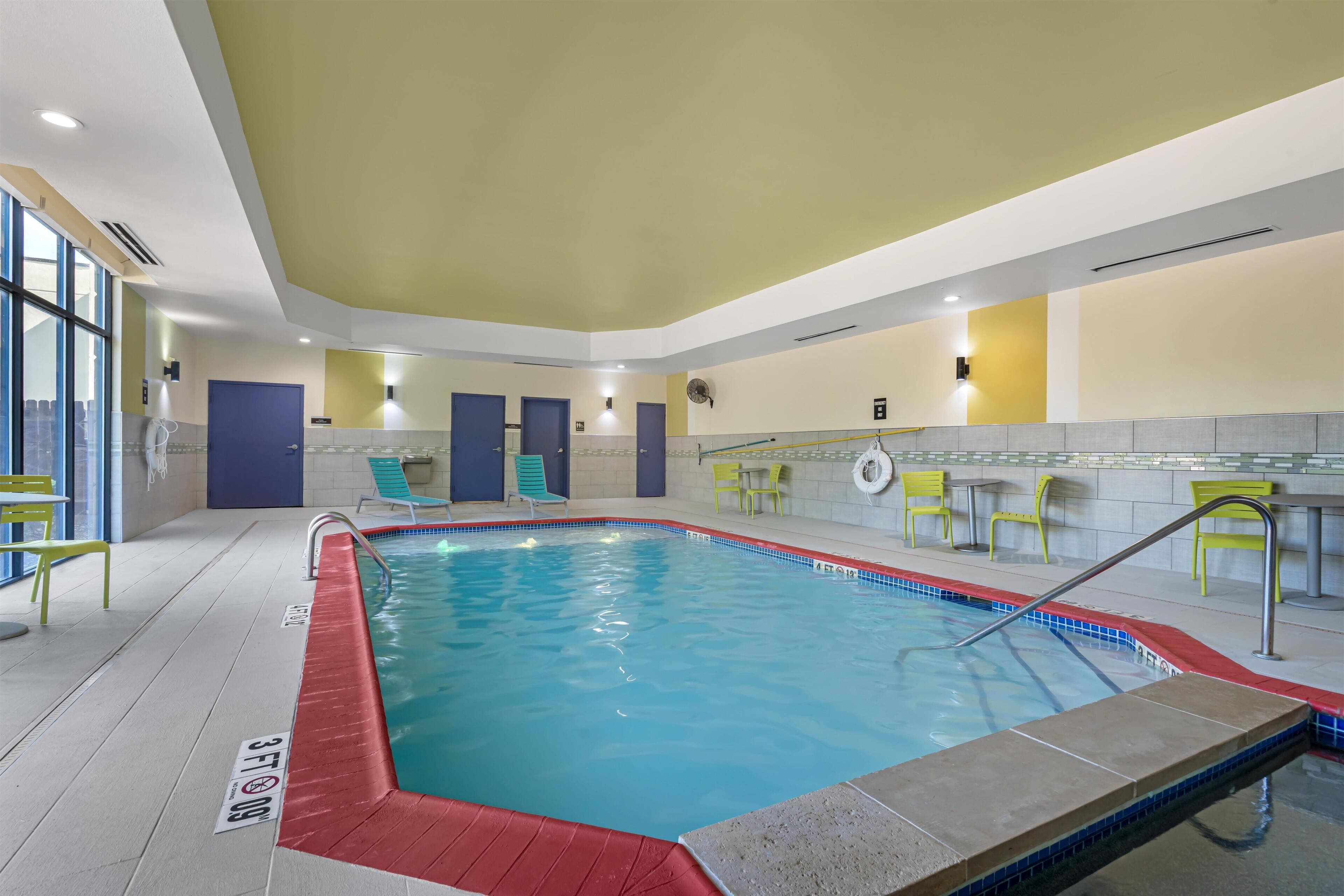Una piscina interior con agua cristalina, rodeada de sillones de descanso y un suelo de baldosas.