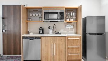 A compact kitchen with a dishwasher, a microwave, a refrigerator, and wooden cabinetry.