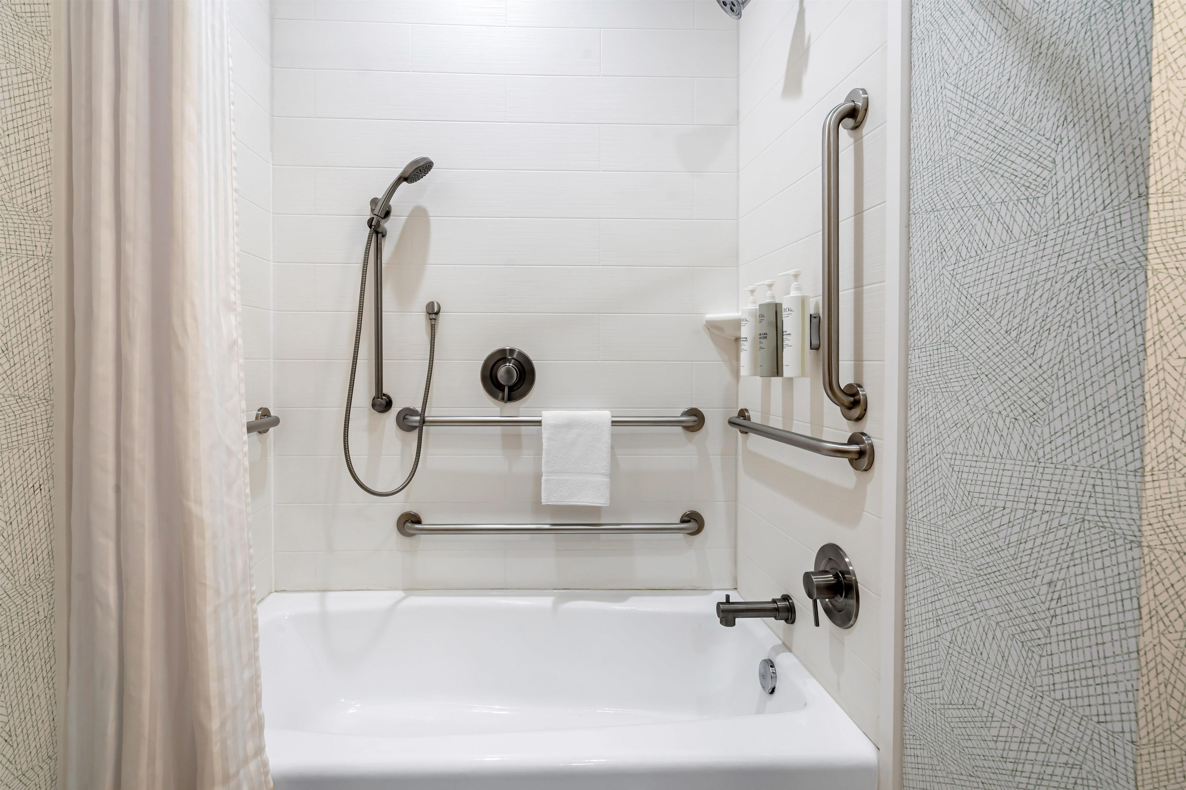 Une salle de bain avec une baignoire blanche, des barres d’appui, une douchette à main et un porte-serviettes.