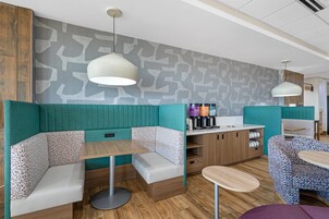 Una cafetería moderna con cabinas y mesas, una estación de café y una pared con diseño.