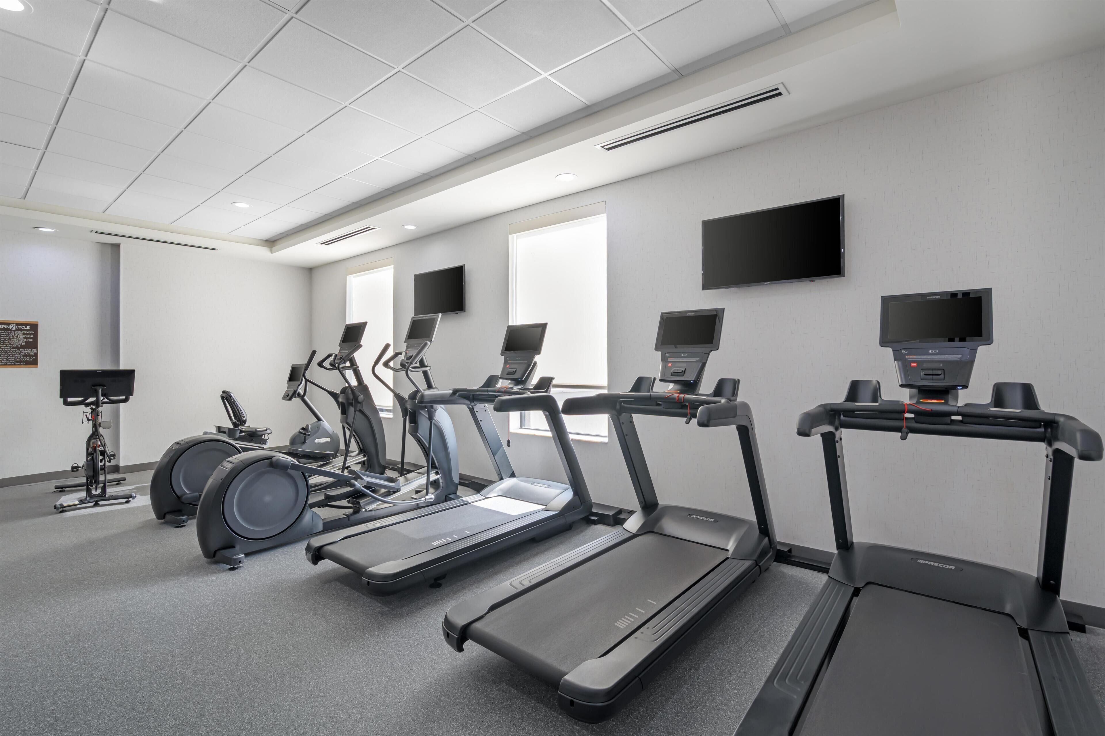 Un gimnasio con cintas de correr, máquinas elípticas y bicicletas estáticas.