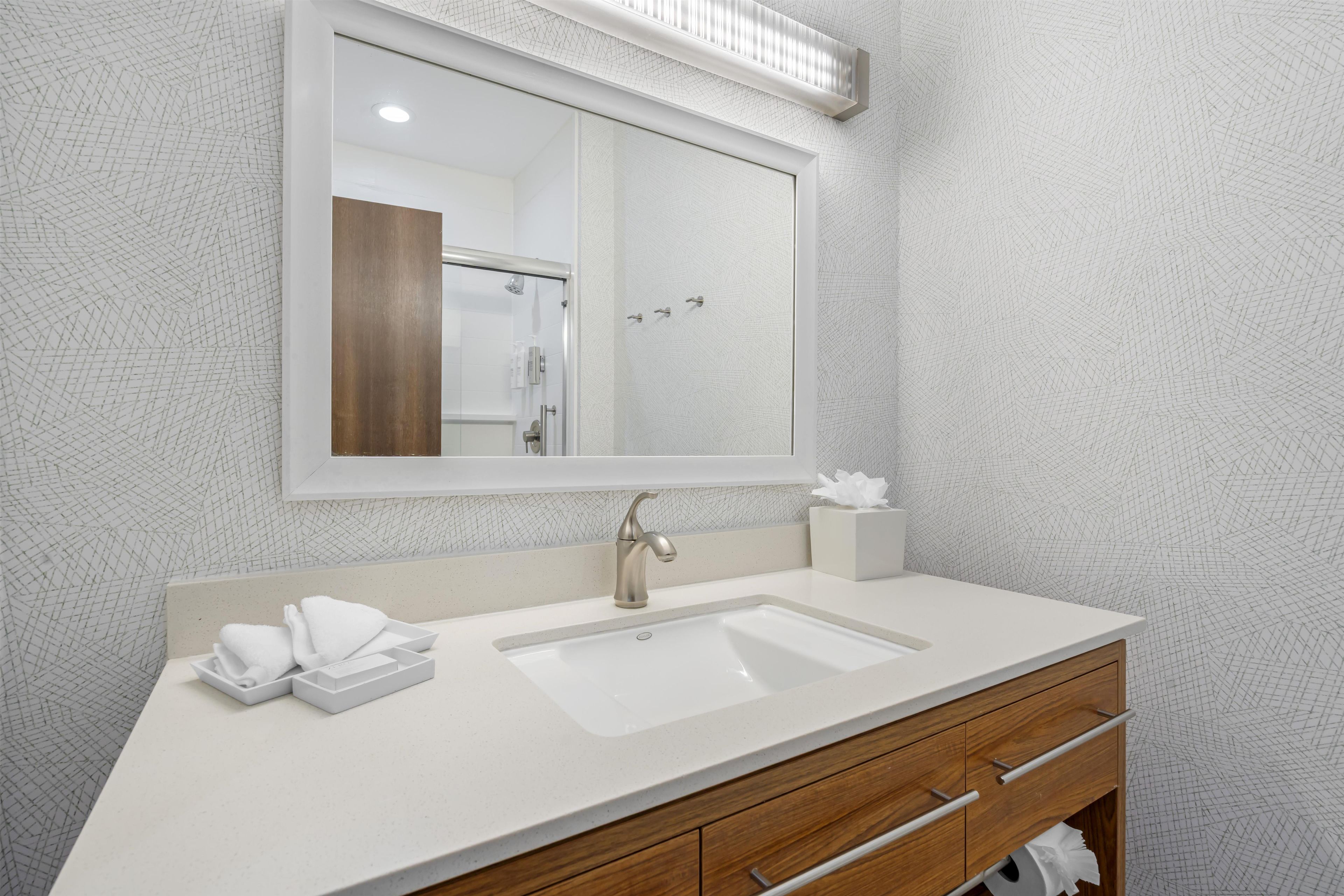 A bathroom with a large mirror, a sink, and a wooden vanity.