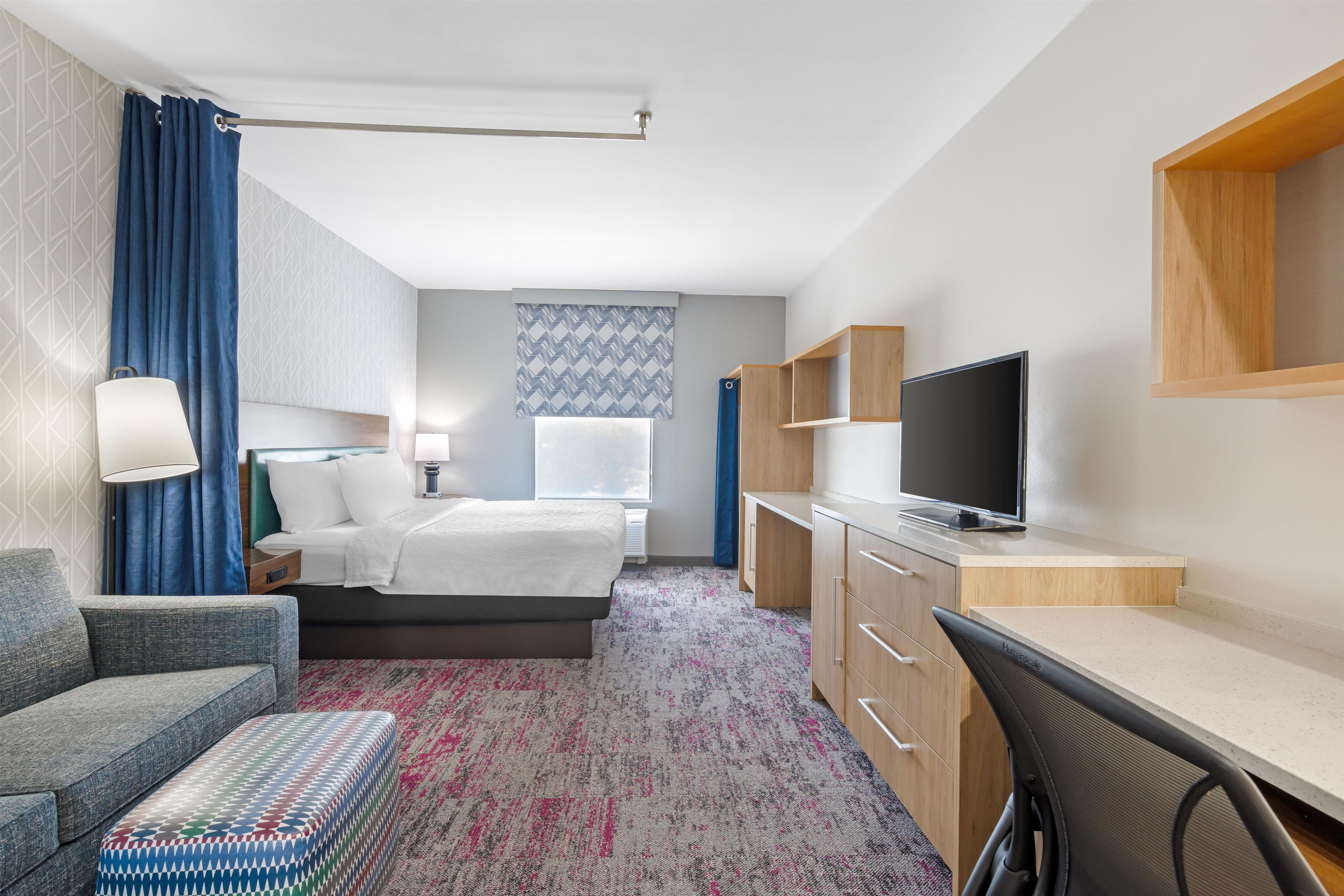 A hotel room with a bed, a desk, a chair, a television, and a window with curtains.