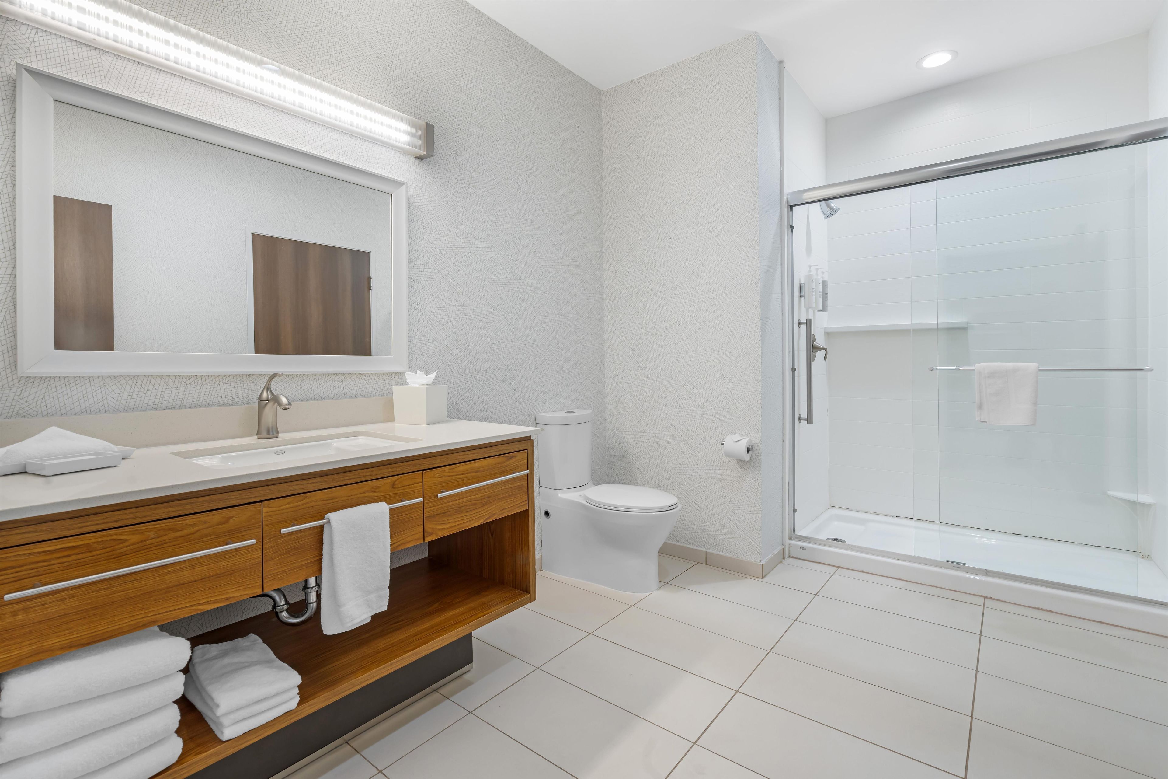 A modern bathroom with a wooden vanity, a large mirror, a toilet, and a glass-enclosed shower.