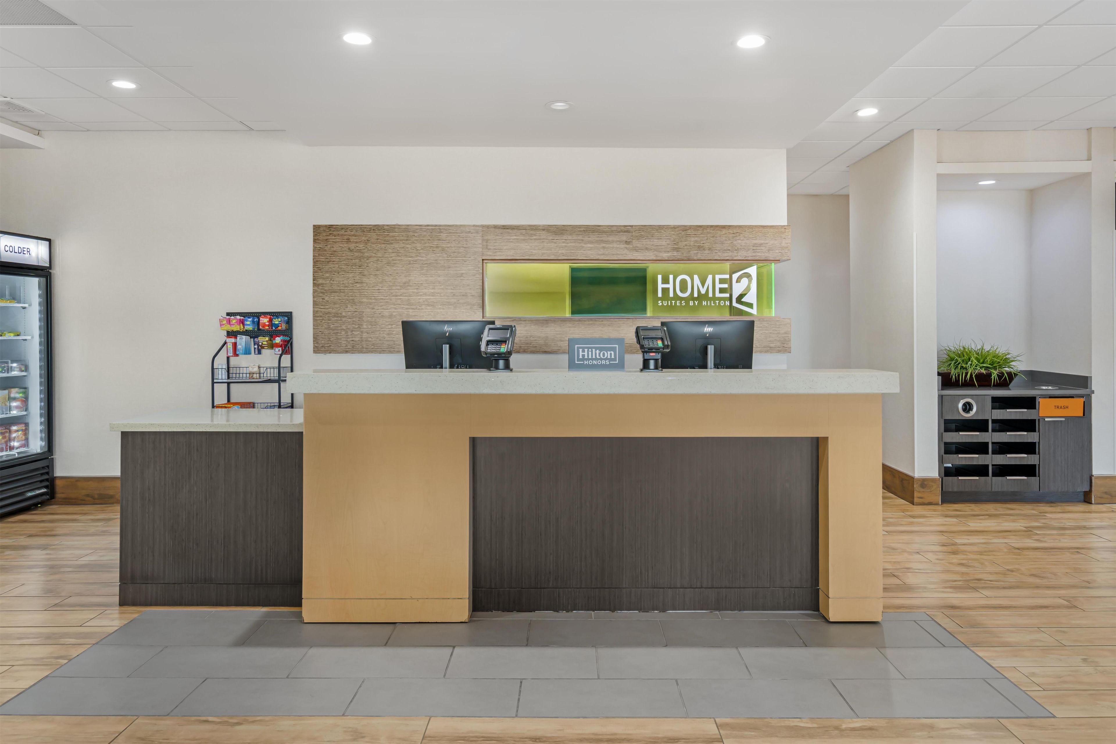 A hotel reception desk with a 'HOME' sign, a minibar, and a trash bin.