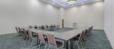 Un salón de conferencias con una larga mesa y sillas, piso alfombrado e iluminación empotrada en el techo.