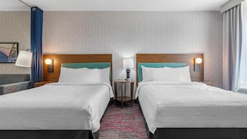 A hotel room with two beds, a small table, a lamp, and a painting on the wall.