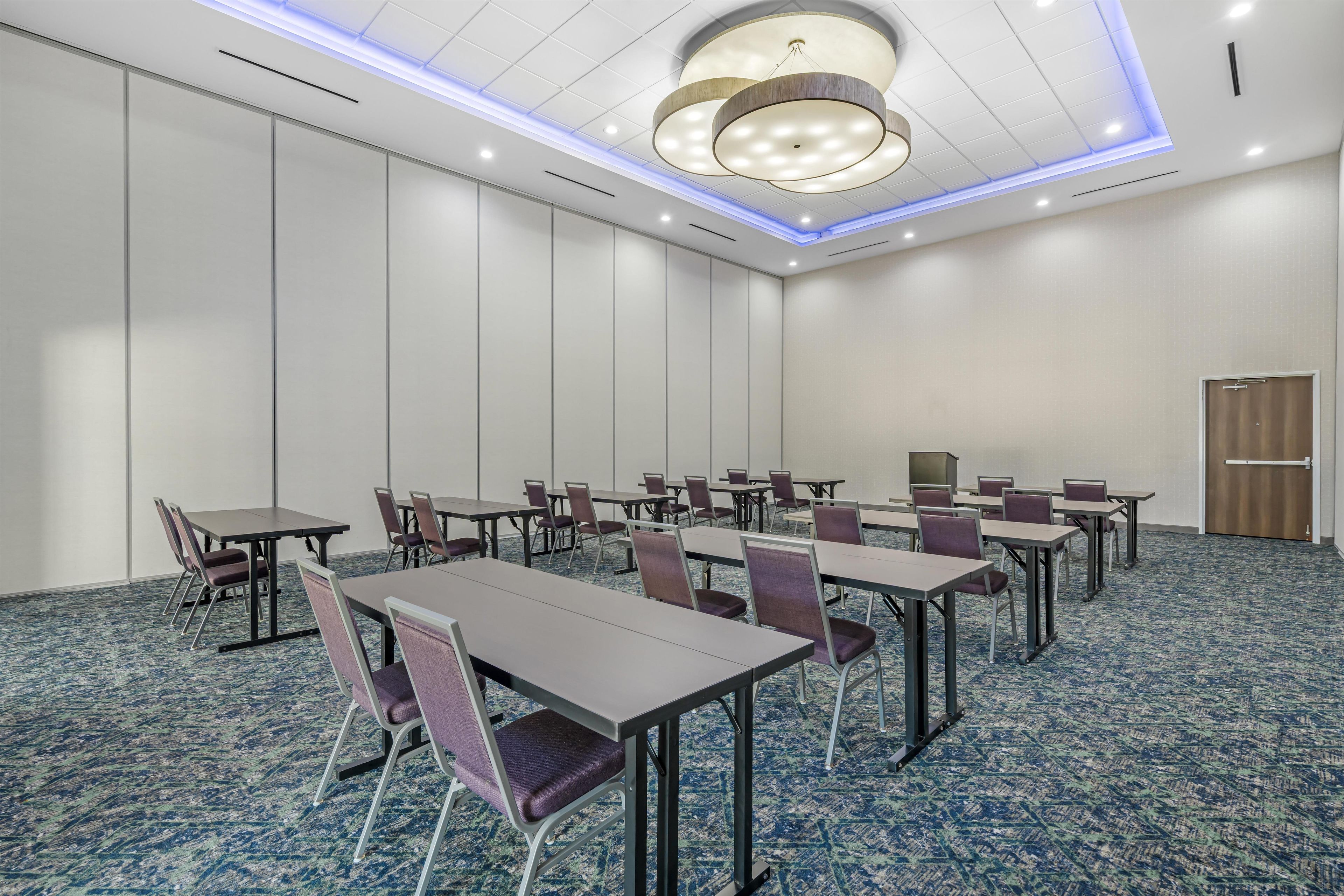 A conference room with tables and chairs, a patterned carpet, and a modern ceiling light fixture.