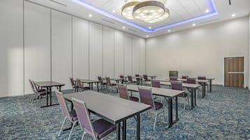A conference room with tables and chairs, a patterned carpet, and a modern ceiling light fixture.