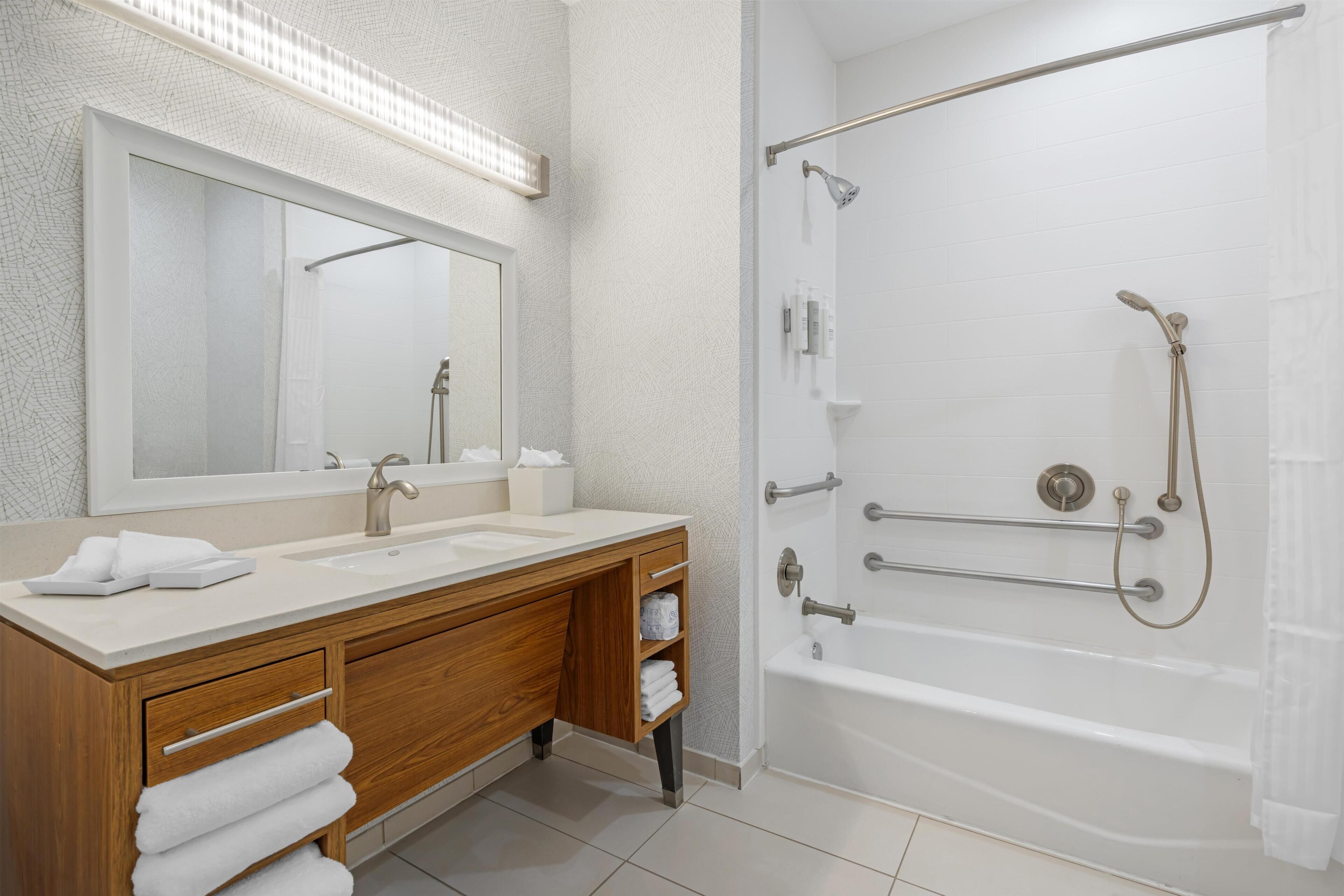 A modern bathroom with a double sink vanity, a large mirror, a shower with a handheld showerhead, and a bathtub.