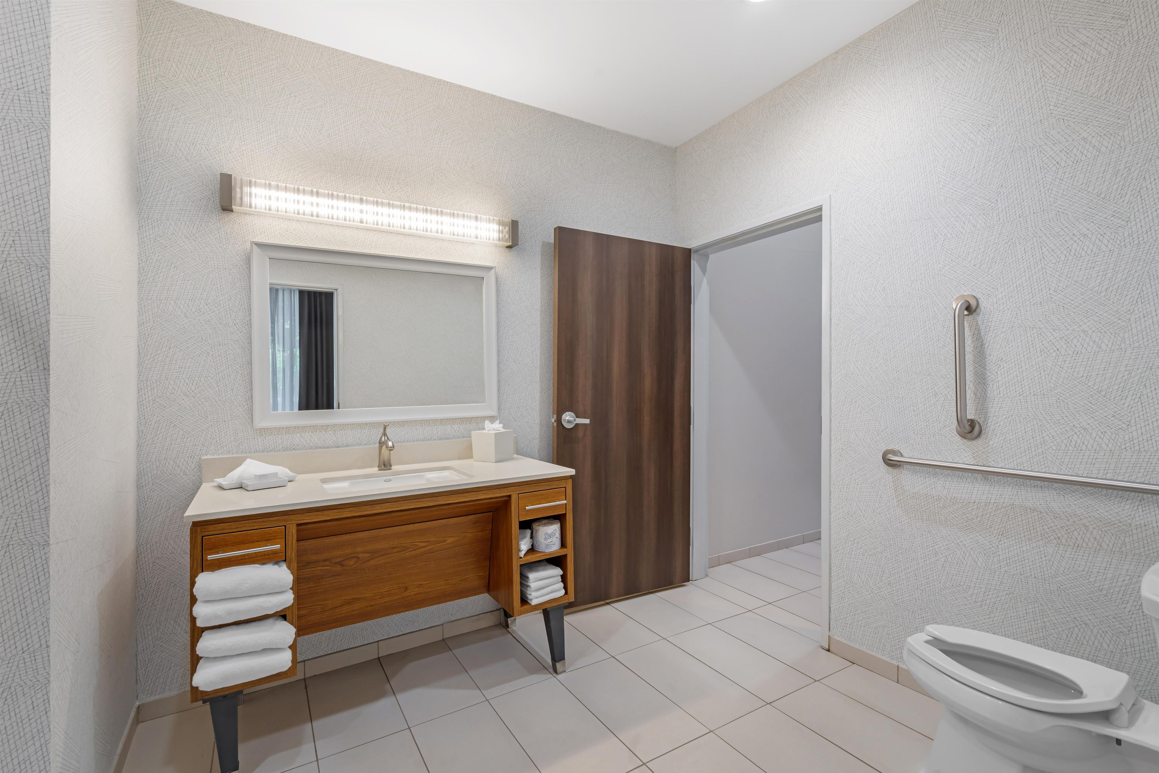 Un baño moderno con tocador de madera, un espejo grande, inodoro y zona de ducha.