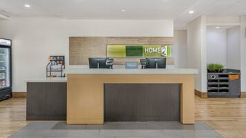 A hotel reception desk with a 'HOME' sign, a minibar, and a trash bin.