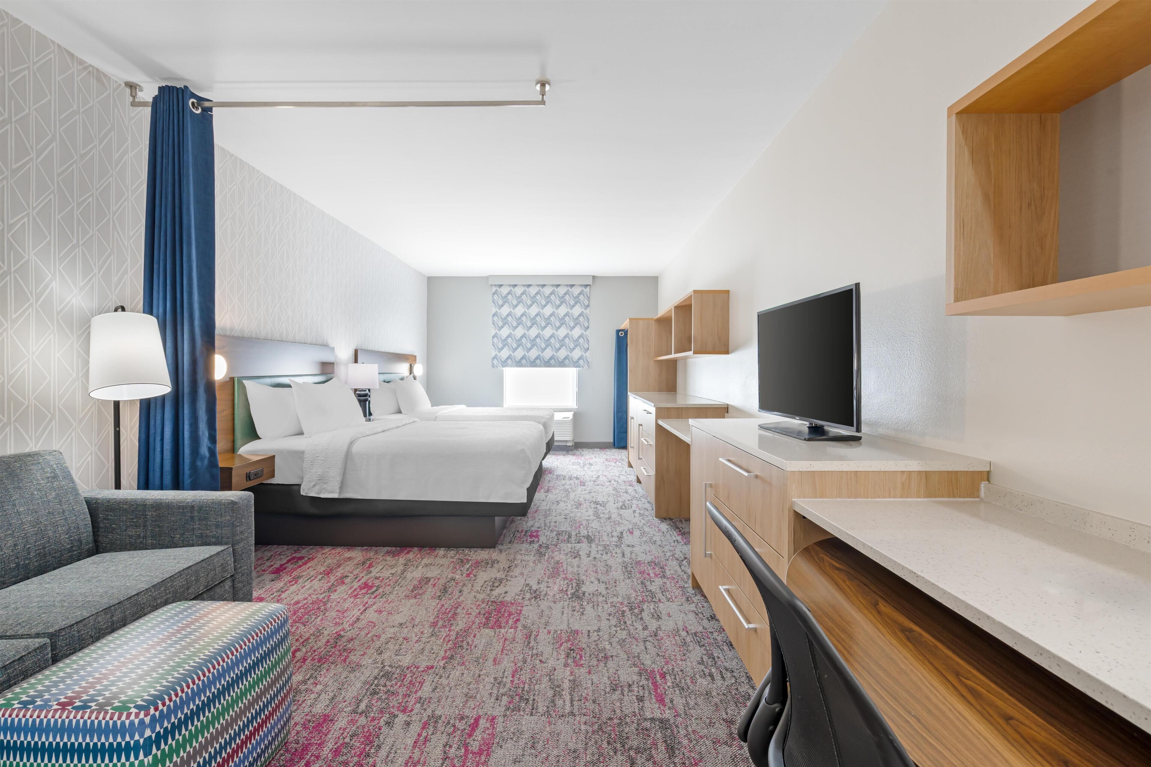 A hotel room with a bed, a desk, a TV, a sofa, and a patterned carpet.