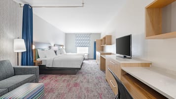 A hotel room with a bed, a desk, a TV, a sofa, and a patterned carpet.