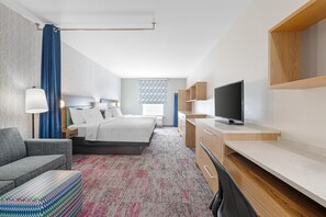 A hotel room with a bed, a desk, a TV, a sofa, and a patterned carpet. - Home2 Suites by Hilton Dallas DeSoto (DeSoto)