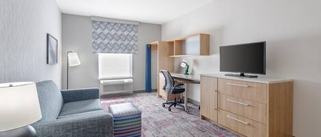 Une chambre d’hôtel moderne équipée d’un canapé, d’un bureau, d’une télévision et d’un tapis à motifs.