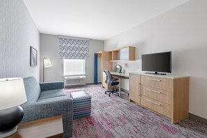 Una habitación de hotel moderna con sofá, escritorio, televisor y una alfombra estampada.