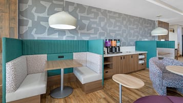 Una cafetería moderna con cabinas y mesas, una estación de café y una pared con diseño.