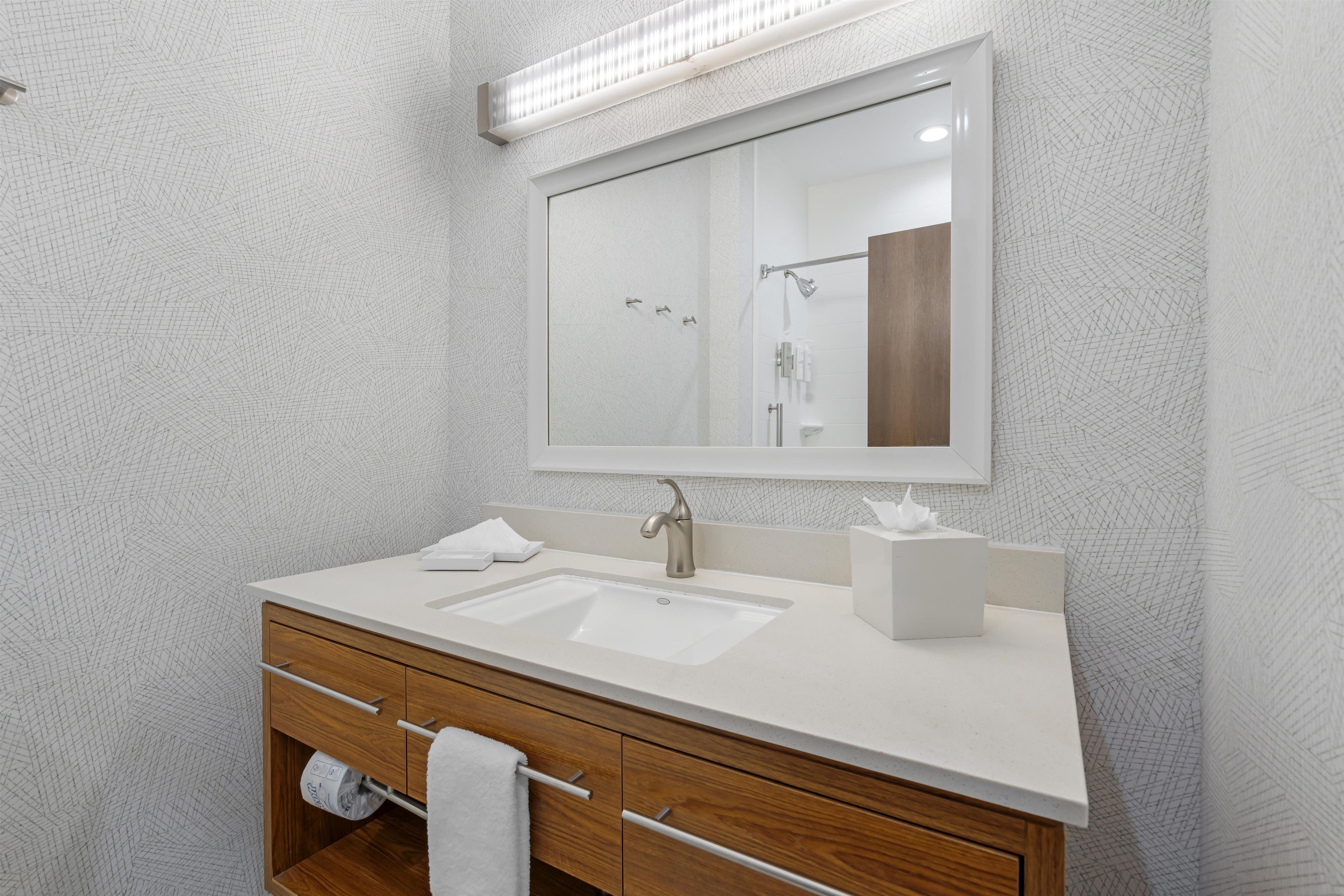 A modern bathroom with a large mirror, two sinks, a wooden vanity, and a towel rack.