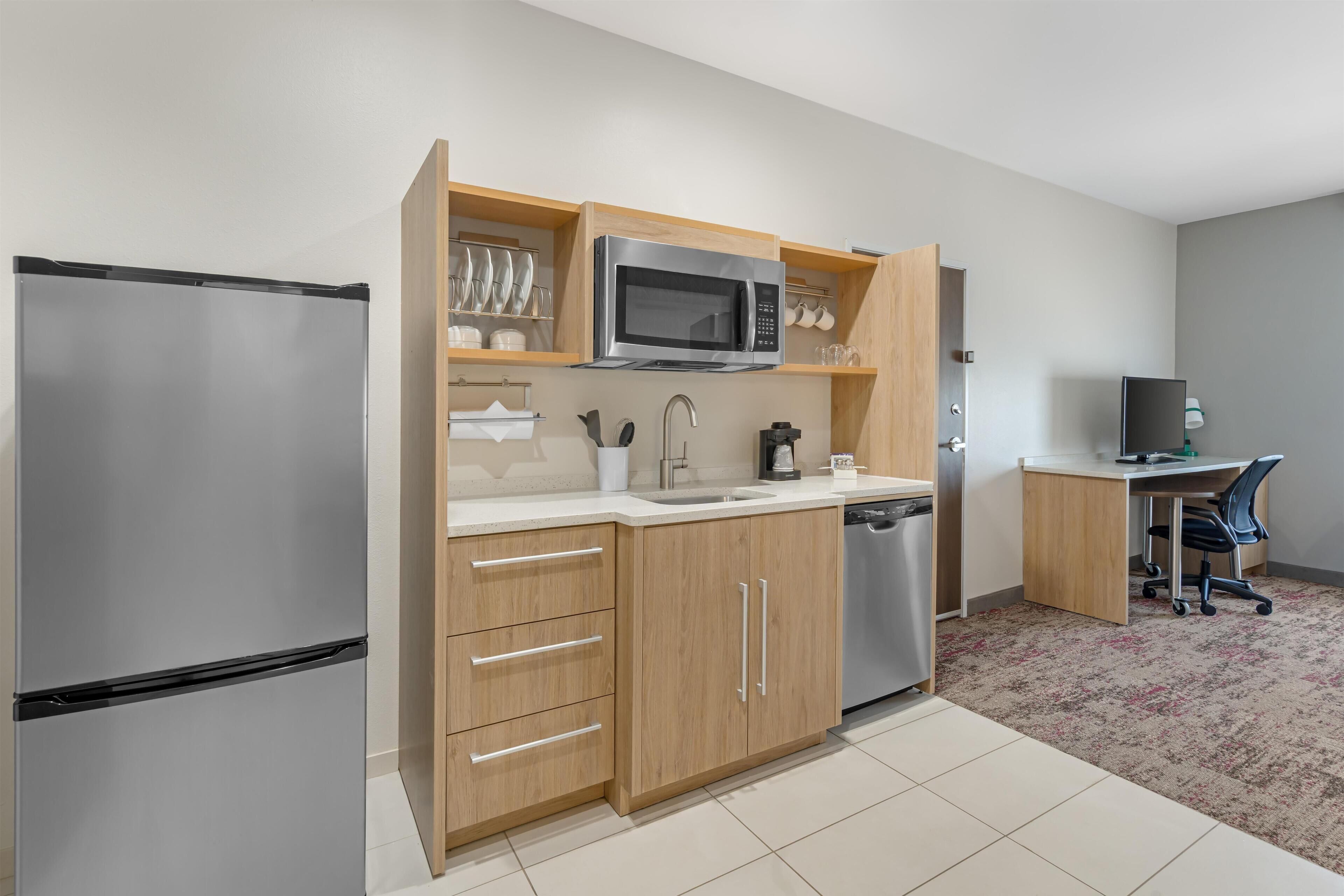 Cocina compacta con refrigerador, microondas, pileta y un pequeño comedor con una silla.