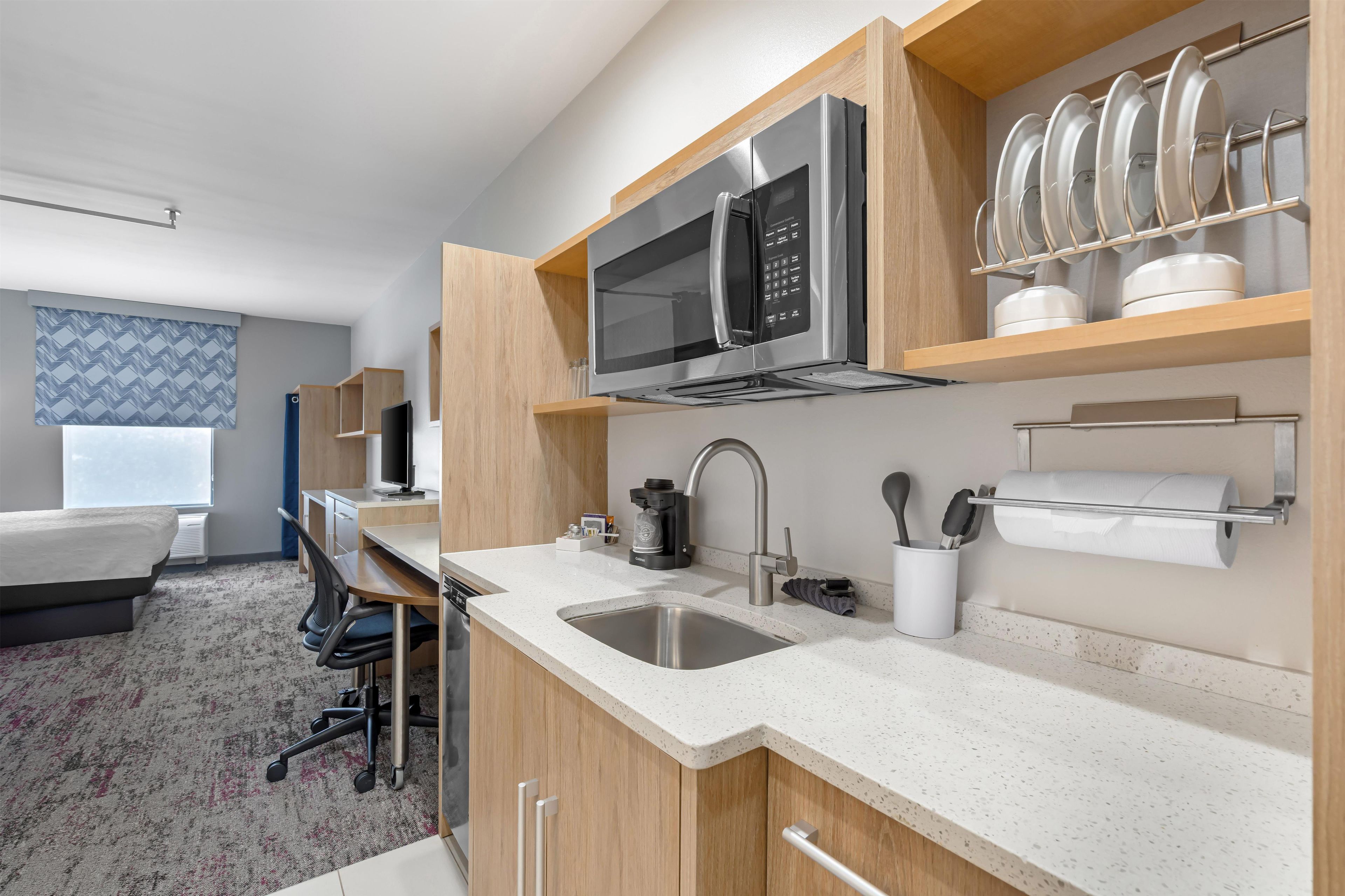 A modern hotel kitchen with stainless steel appliances, a sink, and a dining area with a chair and table.