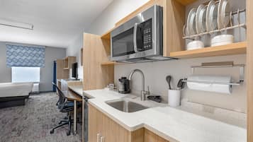 A modern hotel kitchen with stainless steel appliances, a sink, and a dining area with a chair and table.