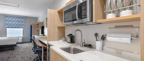 A modern hotel kitchen with stainless steel appliances, a sink, and a dining area with a chair and table.