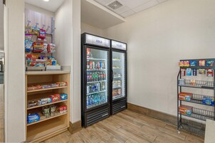 Una sección de aperitivos y bebidas con estantes llenos de diferentes opciones y un refrigerador con bebidas frías.