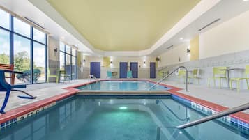Una piscina interior con agua cristalina, rodeada de sillas amarillas y un banco.