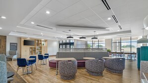 A modern indoor space with seating arrangements, a flat-screen TV, and a view through large windows. - Home2 Suites by Hilton Dallas DeSoto (DeSoto)