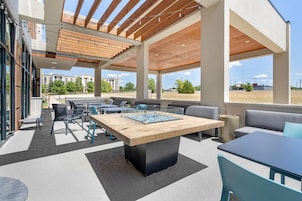 An outdoor patio area with a wooden table, seating, and a view of buildings in the background.