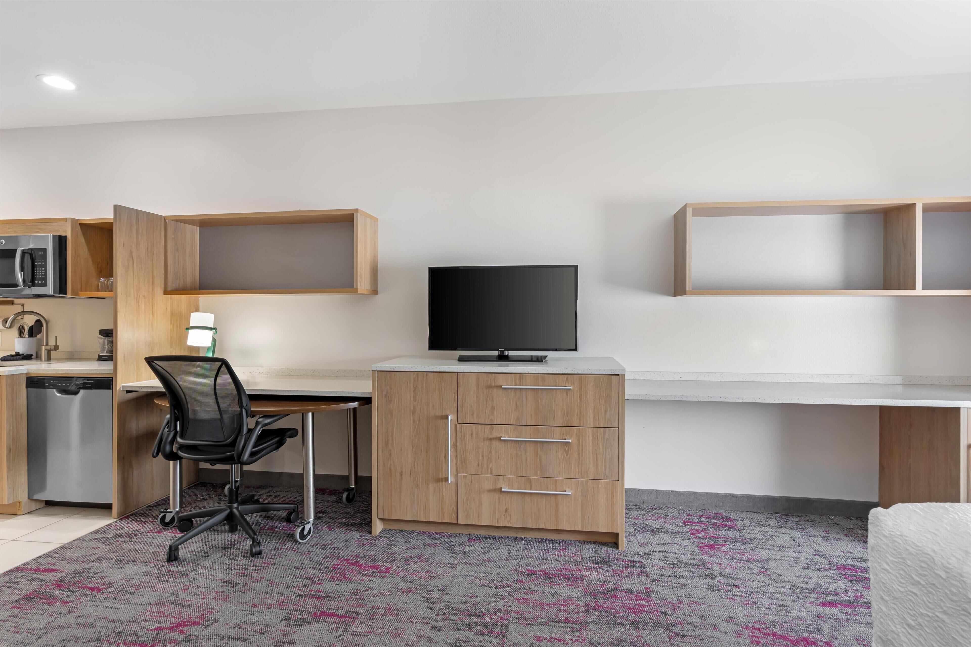 Een moderne, goed verlichte kamer met een bureau, stoel en een televisie.