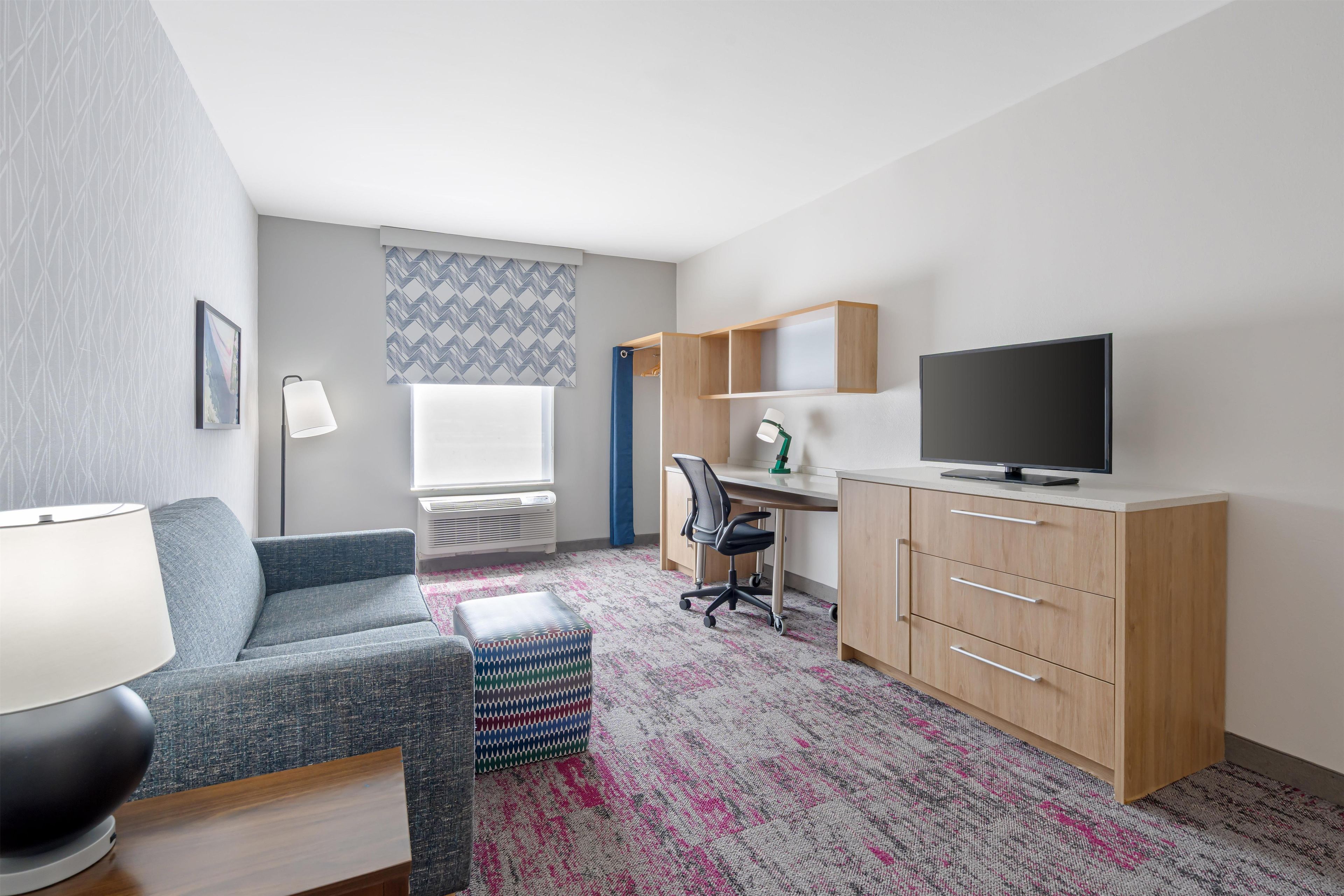 A modern hotel room with a sofa, a desk, a television, and a patterned rug.