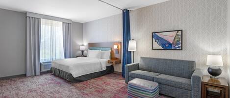 A hotel room with a bed, a sofa, a patterned carpet, a painting, and a window with curtains.