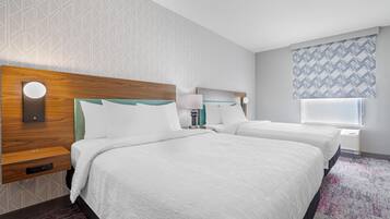 A hotel room with two beds, a wooden headboard, a nightstand, a lamp, and a window with patterned curtains.