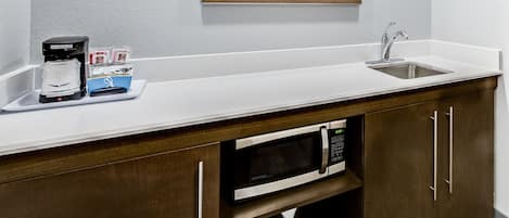 A kitchenette with a coffee maker, microwave, and sink.
