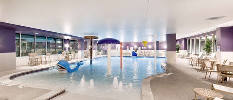 An indoor swimming pool with a blue dolphin decoration, lounge chairs, and tables.