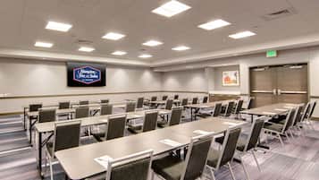 Une salle de conférence équipée de plusieurs tables et chaises, d’un grand téléviseur à écran plat fixé au mur et d’un panneau indiquant la sortie.