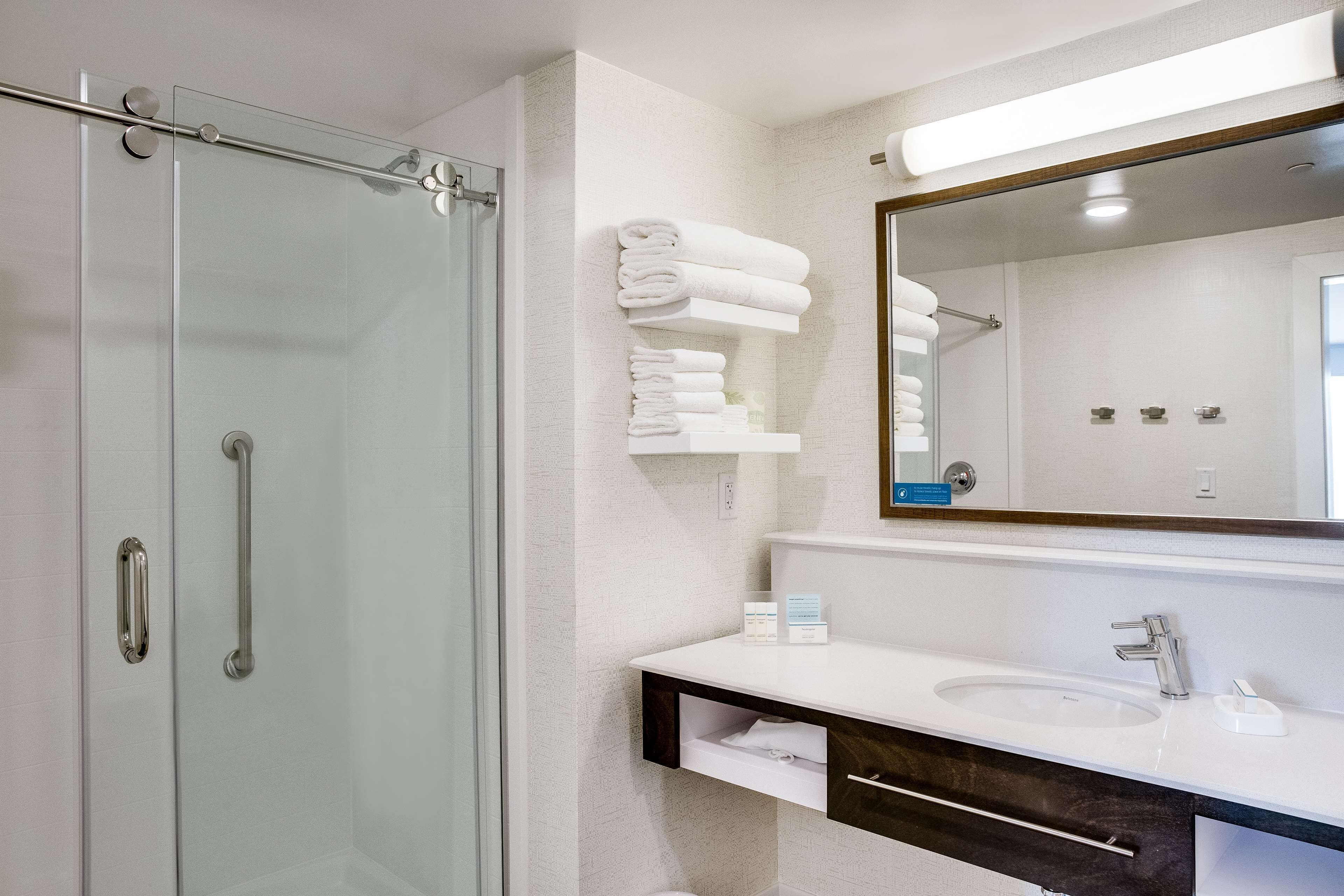 A modern bathroom with a glass shower enclosure, a white sink with a dark countertop, and a mirror above the sink.