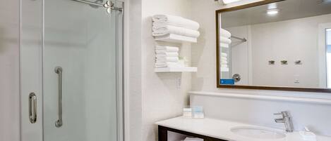 A modern bathroom with a glass shower enclosure, a white sink with a dark countertop, and a mirror above the sink.